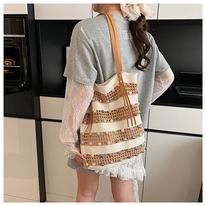 Détail d'un sac cabas en tricot rayé avec perles colorées et anses en cuir marron