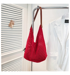Detail of red hollow knit tote bag featuring brown faux leather handles and metal rivets