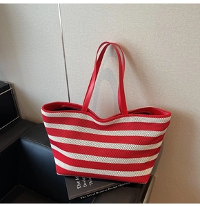 Detail of red and white striped tote bag with red leather handles on a leather sofa