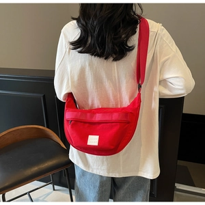 Vue détaillée d'un sac bandoulière rouge en forme de croissant avec patch logo sur modèle