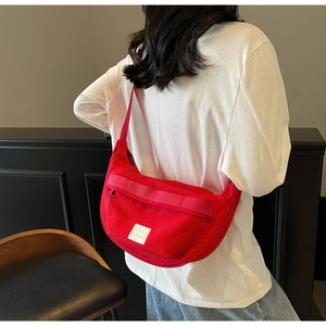 Détail d'un sac bandoulière demi-lune en toile rouge porté par un mannequin en intérieur