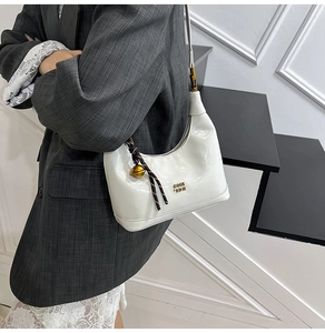Dettaglio borsa hobo in pelle verniciata bianca con logo dorato e ciondolo decorativo