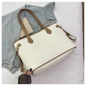 Detailed close-up of a white leather tote bag with brown handles and gold hardware