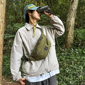 Detail of army green nylon chest bag with woven pullers and adjustable strap in nature