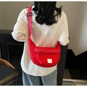 Détail du sac bandoulière en toile rouge avec sangle réglable sur t-shirt blanc