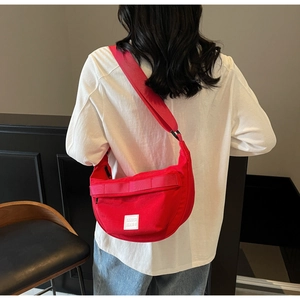 Détail du sac bandoulière demi-lune en toile rouge avec sangle tissée sur un modèle