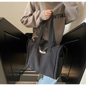 Dettaglio della borsa tote in nylon nero con coulisse laterale e patch logo in pelle
