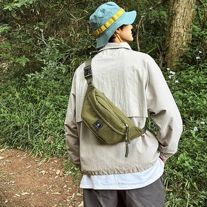 Olive green nylon chest bag with adjustable tactical strap shown in an outdoor setting