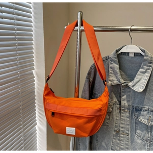 Détail du sac bandoulière orange en nylon avec sangle réglable et poche avant zippée