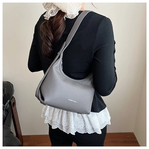 Detailed view of grey lychee leather hobo bag with wide shoulder strap worn by model