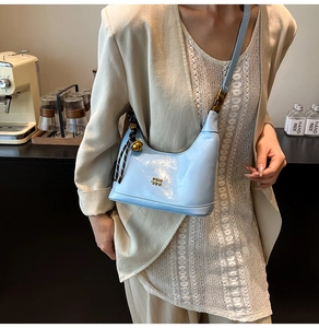 Dettaglio della borsa azzurra in pelle cerata con logo dorato e ciondolo a campanello