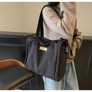 Dettaglio della borsa tote in nylon nero con logo in pelle marrone e tracolla larga