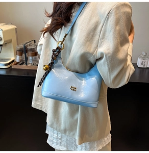 Dettaglio della borsa a spalla azzurra in ecopelle con ciondolo a campana d'oro e logo metallo