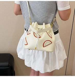 Close-up of cream bucket bag featuring orange fruit appliques and gold hardware details