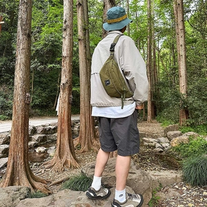 Outdoor scene showing a military green nylon chest bag with adjustable strap and buckle