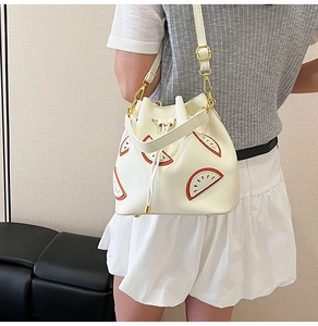 Detail of cream white bucket bag featuring orange fruit appliques and gold-tone hardware