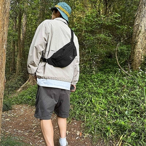 Outdoor view of a black nylon crossbody waist bag worn by a model in a forest