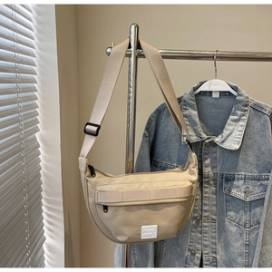 Gros plan du sac bandoulière beige en demi-lune avec poche zippée sur un cintre en métal