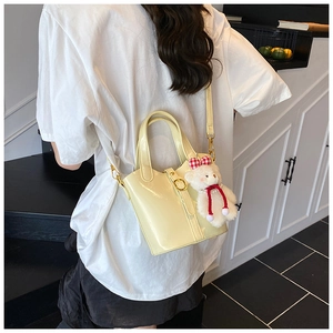 Detail van de crème bucket bag met glanzende afwerking, gesp en schattige berenhanger