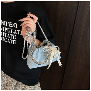 Detail of light blue denim bucket bag with lace bow and pearl chain accessories