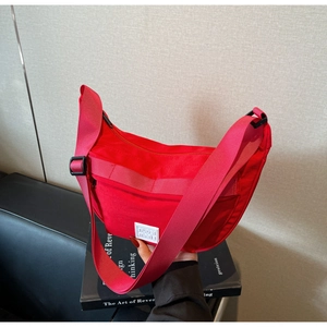 Détail du sac bandoulière demi-lune rouge en nylon avec large sangle et étiquette