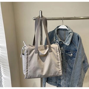 Dettaglio di una borsa tote in tela grigia con patch logo in pelle e coulisse laterale
