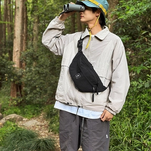Detail of a black sporty chest bag with white logo patch and adjustable strap outdoors