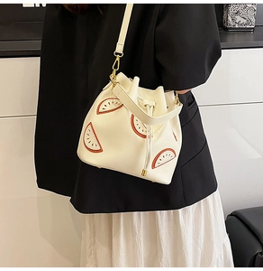 Detail of white bucket bag with orange fruit appliques and gold drawstring hardware