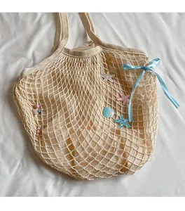 Detail of beige mesh woven tote bag with blue ribbon and seashell beach charms