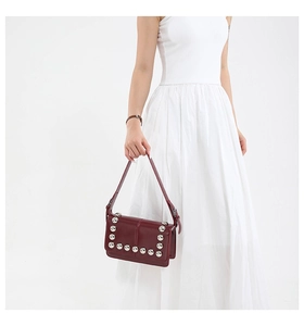 Detail of dark red leather crossbody bag with silver rivet studs and sleek rectangular shape