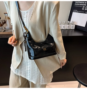 Dettaglio borsa nera in pelle cerata con scritte COIN dorate indossata su un abito beige