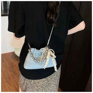 Detail of light blue sequin bucket bag with pearl chain and lace bow on a model