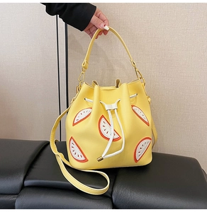 Detail of yellow drawstring bucket bag with decorative fruit patches and gold hardware
