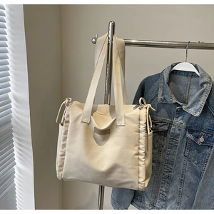 Dettaglio della borsa tote in tela crema con coulisse laterale e patch logo in pelle