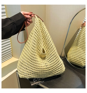 Detail of hollow woven straw tote bag with brown leather handles in indoor light