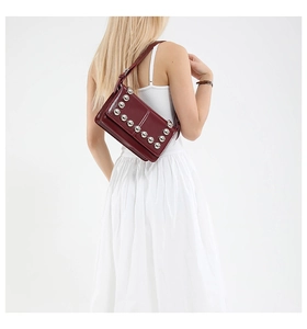 Detail of burgundy patent leather bag featuring large silver metal rivets and strap