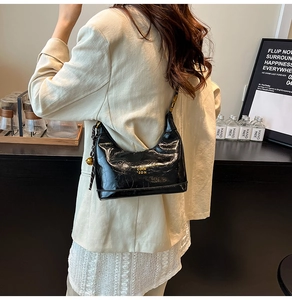 Dettaglio borsa hobo in pelle cerata nera con logo dorato e ciondolo a campanello