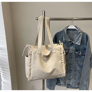Dettaglio della maxi borsa tote crema con bordi arricciati e logo in pelle su denim