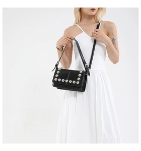 Close-up of black glossy leather bag featuring silver beaded rivet trim on the flap