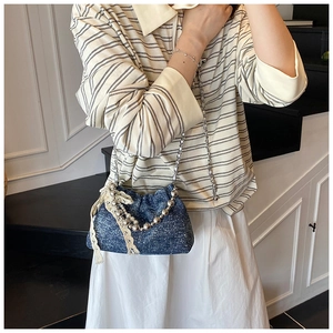 Detail of blue denim bucket bag featuring pearl chains and cream lace bow accents