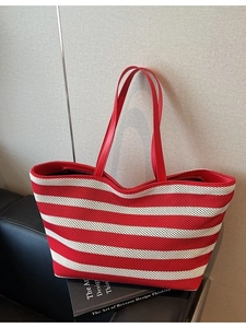 Large red and white striped knit tote bag with red faux leather handles on a minimal background