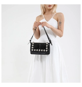 Detailed view of black leather shoulder bag with silver rivets worn by model in white dress