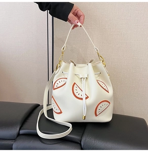 Close-up of white drawstring bucket bag featuring orange slice embroidery and gold hardware