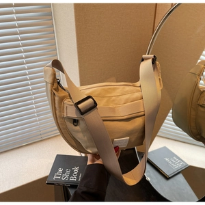 Détail du sac bandoulière beige en demi-lune avec large sangle et logo apparent
