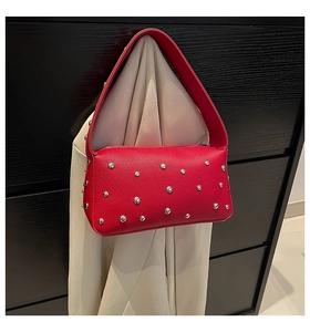 Detail of red leather shoulder bag with silver studs hanging on a beige blazer jacket
