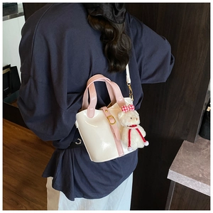 Detail van roze en witte emmer tas met een pluchen beer bedeltje en glanzende afwerking