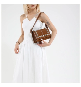 Detail of brown leather crossbody bag featuring silver rivet studs and adjustable strap