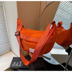 Détail du sac bandoulière demi-lune en nylon orange avec sangle noire réglable et logo blanc