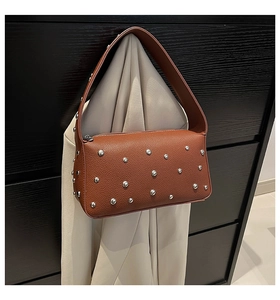 Detail of brown pebbled leather baguette bag with silver studs on strap and body