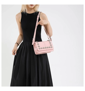 Close-up of pink glossy leather shoulder bag with silver studs on model in black dress